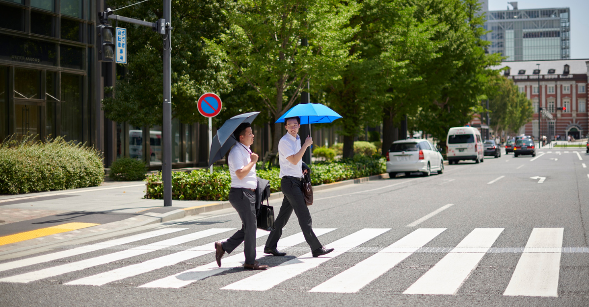 Businessmen crossing a zebra striped crosswalk with umbrellas